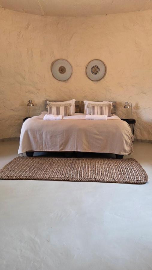 Una camera dai muri arrotondati e intonacati, con un letto matrimoniale, due dischi decorativi alla parete e un tappeto intrecciato