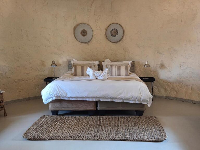 Un letto matrimoniale sotto due dischi decorativi, tra due lampade da comodino, con un tappeto intrecciato