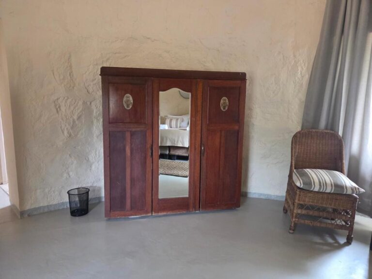 Un armadio in legno scuro con anta a specchio e una poltrona in rattan, in una camera dai muri intonacati