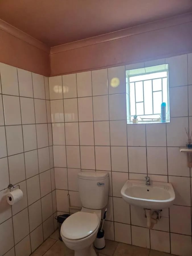 Un bagno piastrellato di bianco, con WC, lavabo e una finestrella