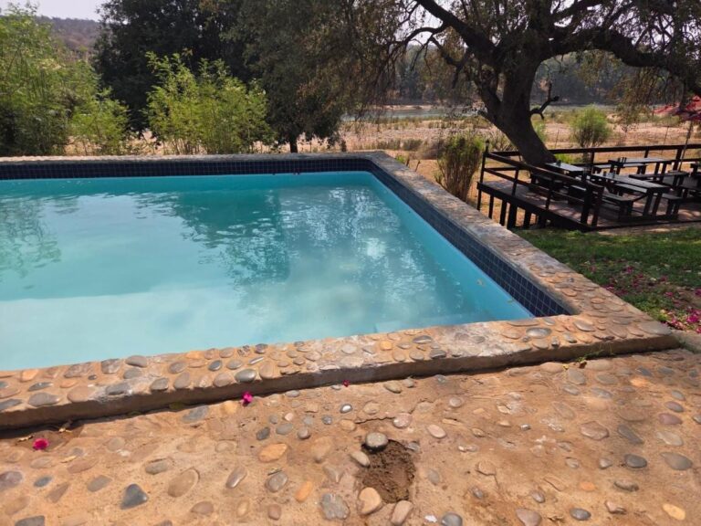 La piscina bordata di ciottoli del Three Bridges B&B, davanti a una terrazza in legno con tavoli da picnic e al fiume