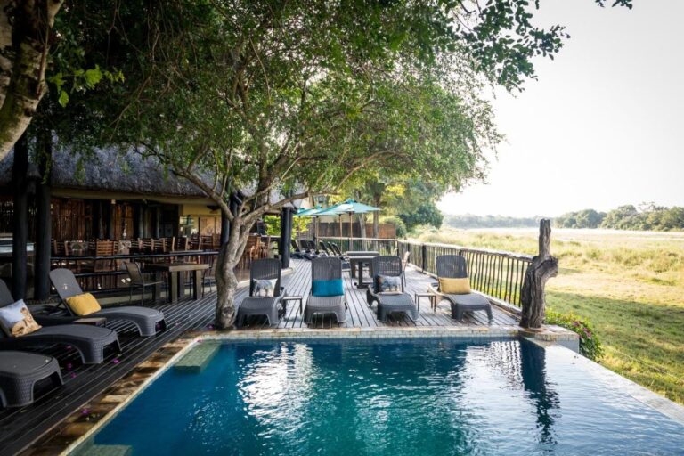 La piscina dell'Umkumbe Safari Lodge e la sua terrazza in legno, sopra la riva erbosa del fiume