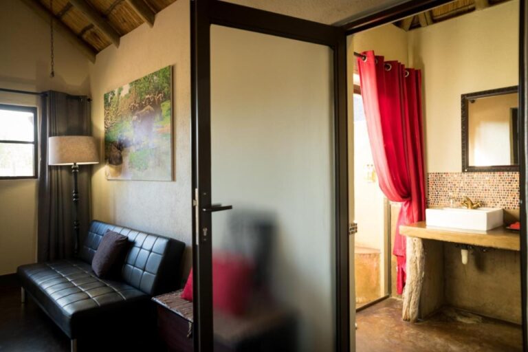 L'angolo salotto di una camera, con un divano in pelle nera, e il bagno dietro una porta a vetri