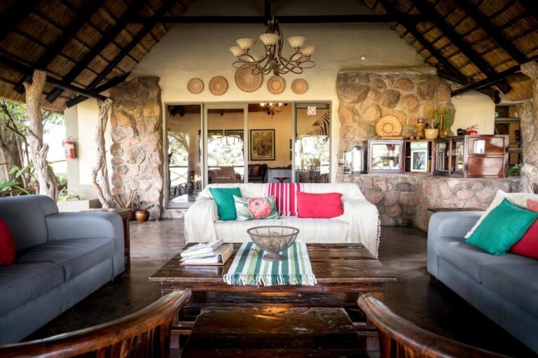Il salone aperto dell'Umkumbe Safari Lodge, sotto la paglia, con divani grigi e muri di pietra